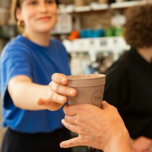 Barista tendant une tasse réemployable Billie Cup à un client