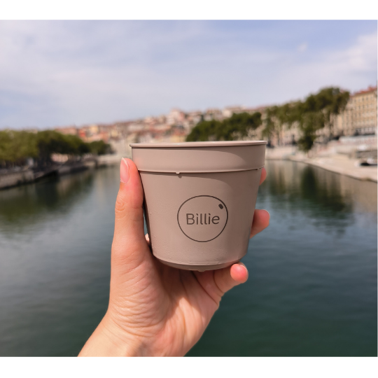 Main qui tient une tasse réutilisable Billie 20 devant un paysage urbain, à Lyon